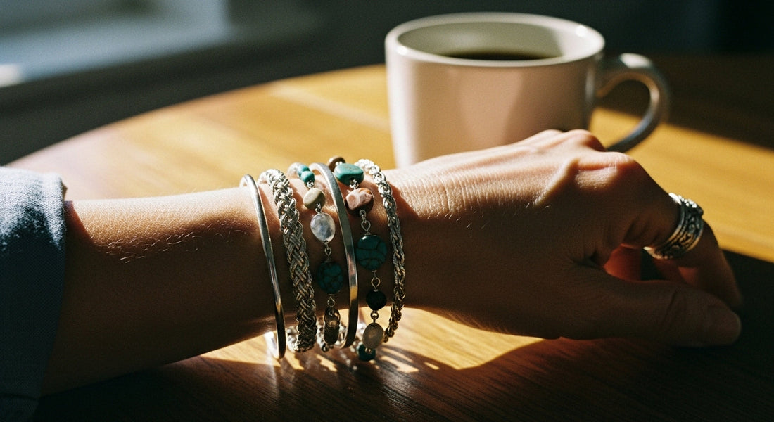 A close-up of a mature white woman’s wrist wearing several elegant stack bracelets made of silver, rope, and natural stones