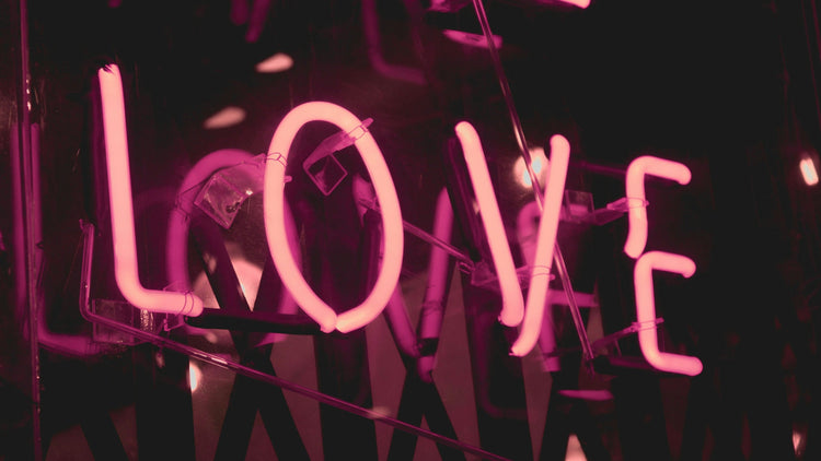 A close-up of a glowing neon sign that reads 'LOVE' in bright pink, set against a dark background, symbolizing romance and affection