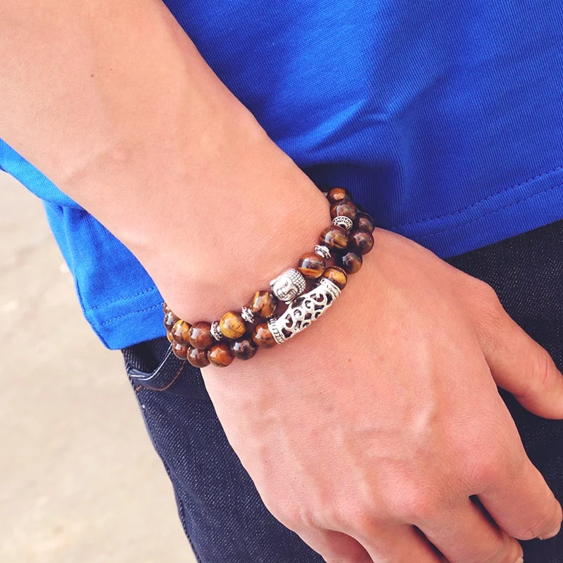 A close-up of a wrist wearing a tiger's eye bead bracelet with a silver Buddha charm, illustrating casual style