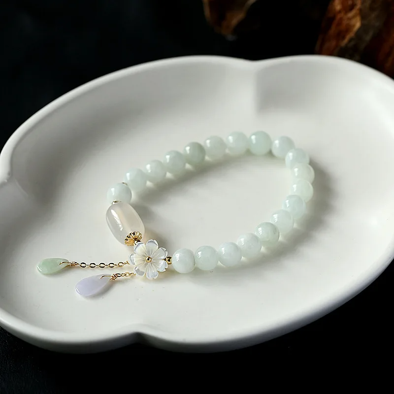 Close-up of white jade bead bracelet featuring intricate floral charm and translucent stone pendants