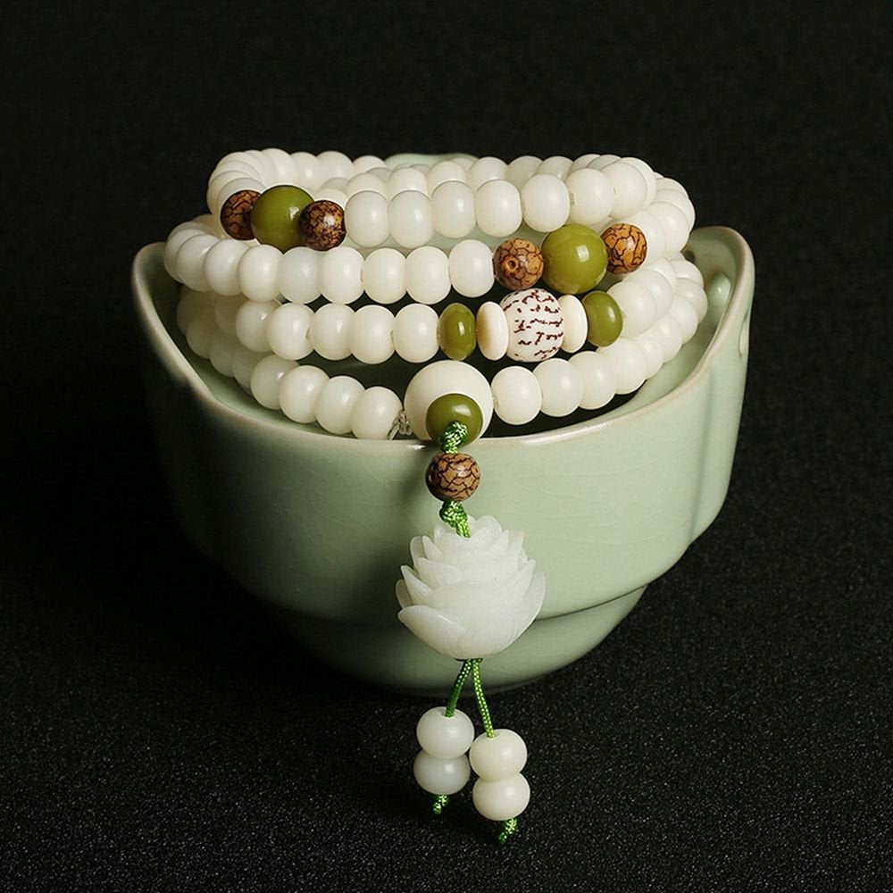 Ornate white beaded jewelry piece with green accents against a dark backdrop