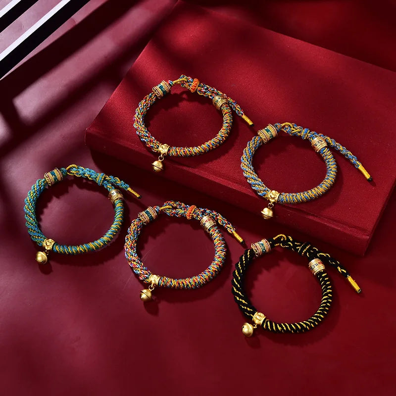 Five colorful Tibetan Ethnic Hand-woven Rope Bracelets with bells arranged on burgundy surface